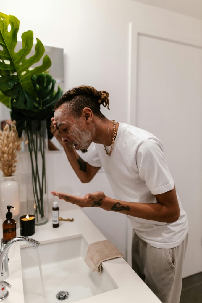 Male washing face with skincare products by a sink. Indoor wellness and grooming scene.