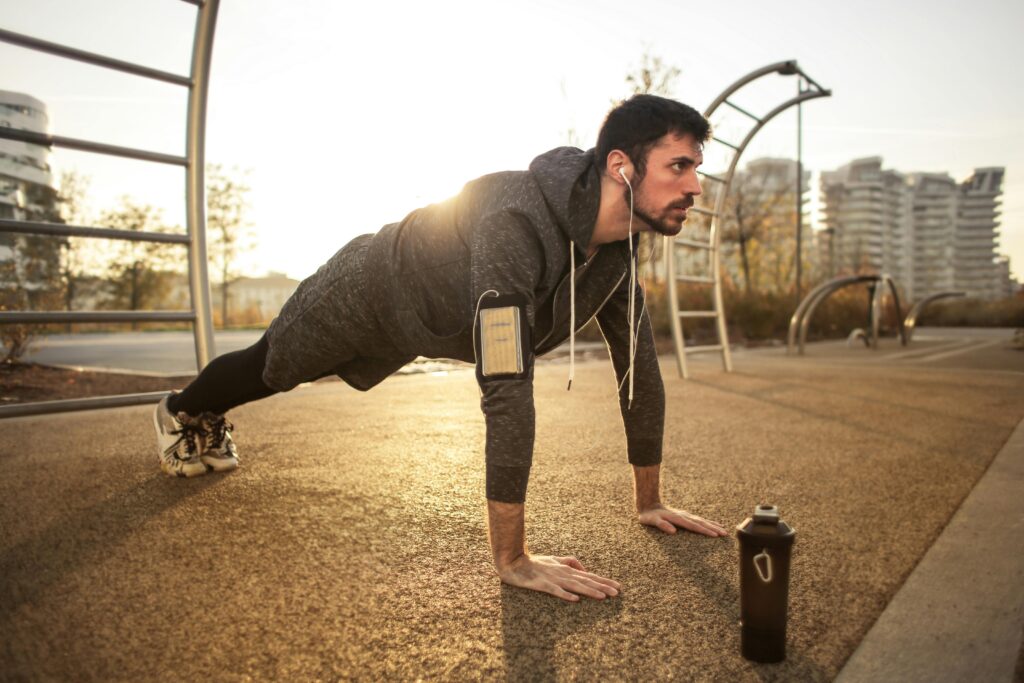 Adult man doing push-ups outdoors with earphones during sunrise, showcasing fitness and healthy lifestyle.