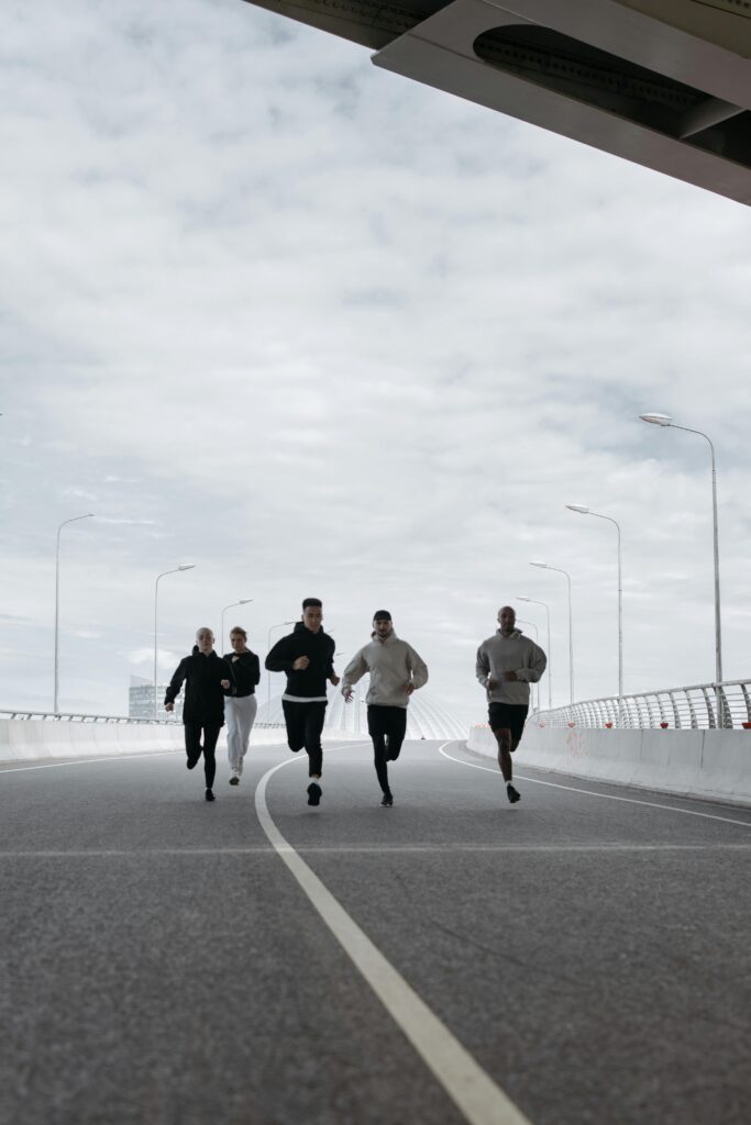 A diverse group of friends jogging on a bridge under a cloudy sky, promoting fitness.